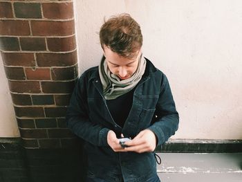 Mid adult man standing against brick wall in city