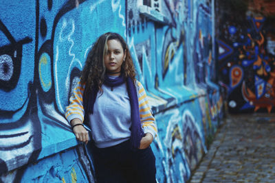 Portrait of young woman standing by graffiti wall