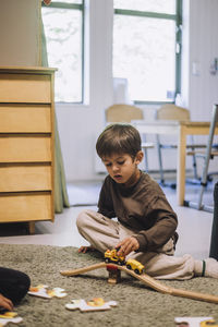 Boy playing with toy train while sitting on carpet in kindergarten