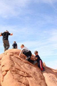 Low angle view of people on rock formation against sky