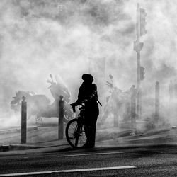 Silhouette woman riding bicycle on road in city