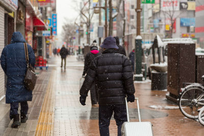 Rear view of people walking on wet street in city