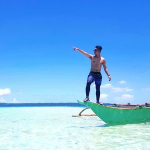 Full length of shirtless man standing on boat at sea against blue sky