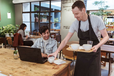 Mid adult owner serving coffee to male customer at cafe