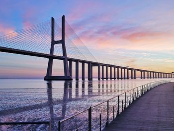 Bridge over tagus river against sky with a beautiful sunrise from a pier at nations park lisbon