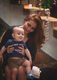 Portrait of son with mother sitting on chair at home