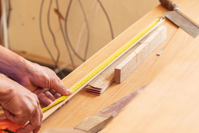 Cropped hands measuring wood on table