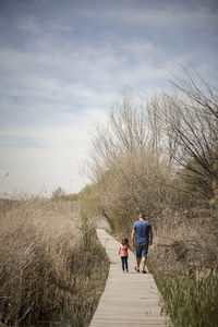 Rear view of father and daughter walking on boardwalk in forest