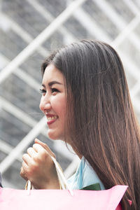 Side view of smiling young woman holding shopping bags