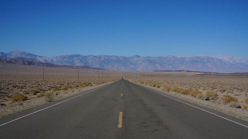 Road leading towards mountains against clear blue sky