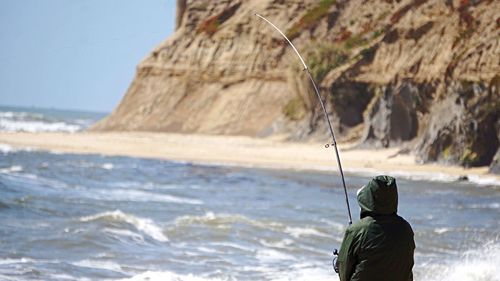 Rear view of person fishing on beach against clear sky