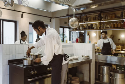 Male and female chefs cooking food at commercial kitchen in restaurant