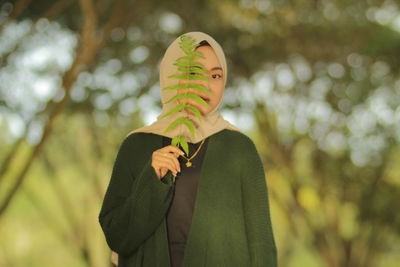 Portrait of woman in hijab holding fern standing outdoors