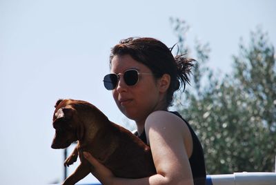 Side view of young woman carrying puppy while standing against clear sky