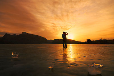 Silhouette mature man standing on frozen lake against sky during sunset