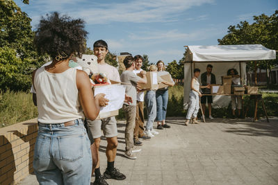 Team of male and female volunteers passing donation goods in boxes while standing in row during charity drive at communi