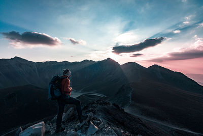 Hiker with backpack standing on cliff against sky during sunset