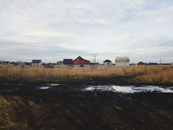 Houses on field by river against sky