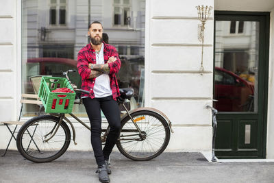 Portrait of owner with arms crossed leaning on bicycle outside candy store