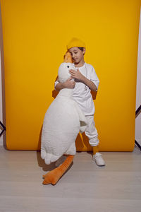 Photo session of a boy in a yellow hat and white t-shirt with a toy bird goose hugging standing 