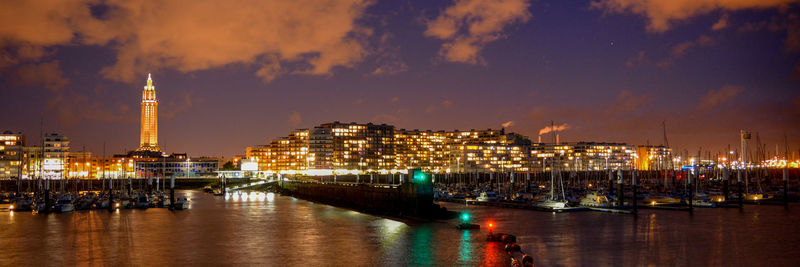 Panoramic view of illuminated cityscape by river against sky at night