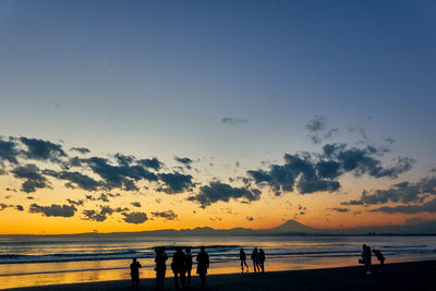 Silhouette people on beach against sky during sunset