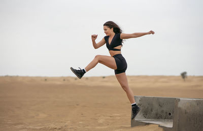 Full length of woman jumping while running on sand