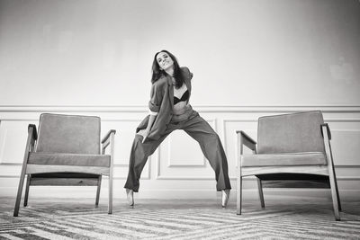 Ballerina in a gray striped suit stands between the chairs on pointe shoes in a plie