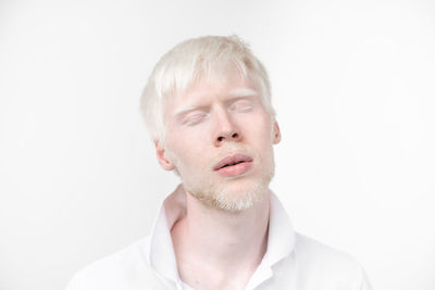 Close-up of man with eyes closed standing against white background