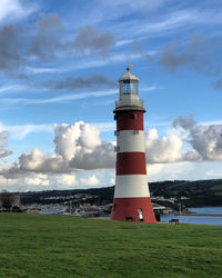 Lighthouse on field by building against sky