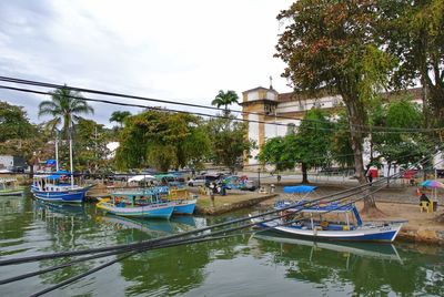 Boats moored in canal by city against sky