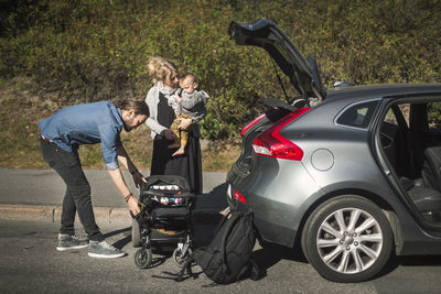 Mid adult parents with son and baby carriage near car on street