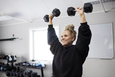 Smiling woman exercising with dumbbells at health club