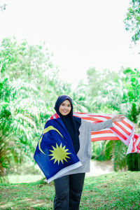 Portrait of young woman standing against trees
