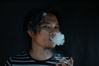 Close-up of young man smoking cigarette against wall