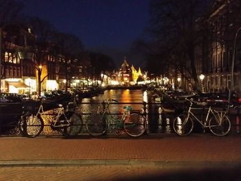 Bicycles by illuminated city against sky at night