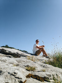 Man sitting on rock against clear blue sky