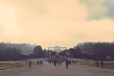 People on road at schonbrunn palace against cloudy sky