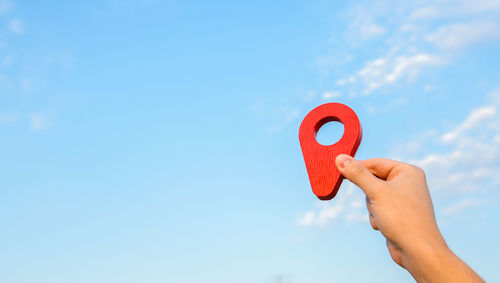 Cropped hand holding heart shape against blue sky