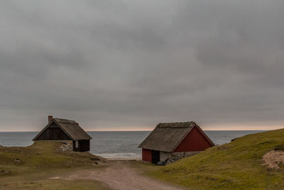 Huts at sea shore against cloudy sky
