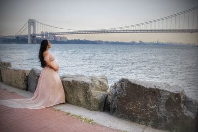 Side view of pregnant woman standing by retaining wall against bridge