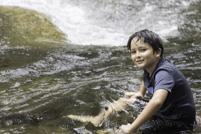 Side view of boy standing on rock by river