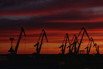 Silhouette cranes at construction site against sky during sunset