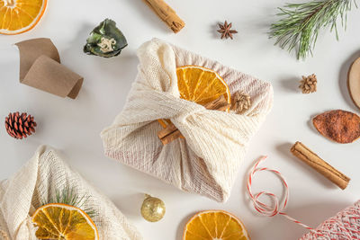 Christmas gift in linen fabric with oranges on white table. furoshiki gift. xmas presents in clothes