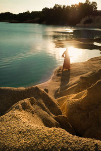 Woman sitting at beach against sky during sunset
