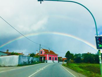 Rainbow over road by building against sky