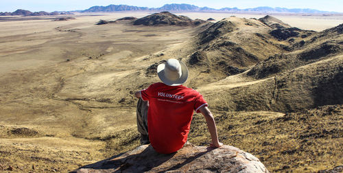 Rear view of man sitting on rock against landscape