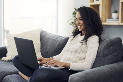 Young woman using phone while sitting on sofa at home