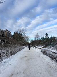 Rear view of man walking on snow covered field against cloudy sky