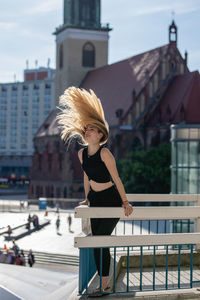 Beautiful young woman tossing hair on balcony against buildings in city